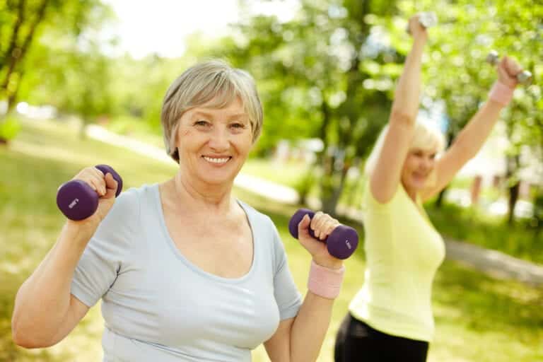 Two senior women lifting weights outside in summer