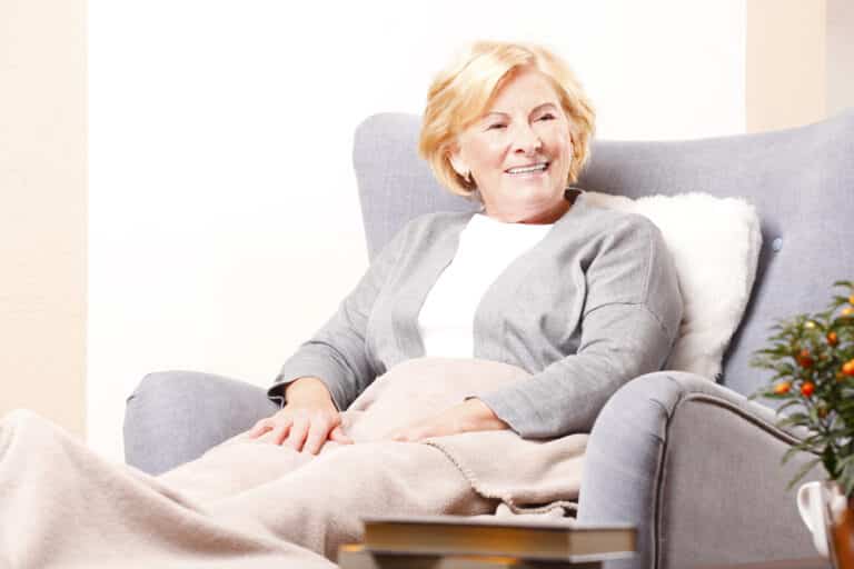 Senior woman smiling at home, sitting in armchair with blanket on her lap