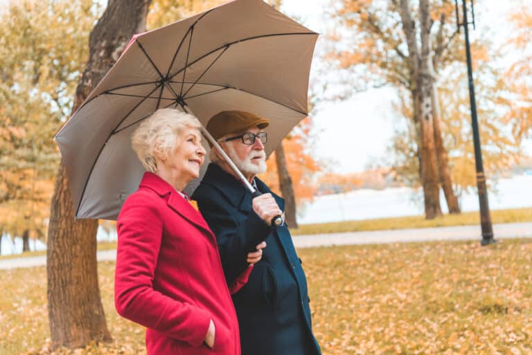 Two seniors on a walk in the park in autumn with an umbrella