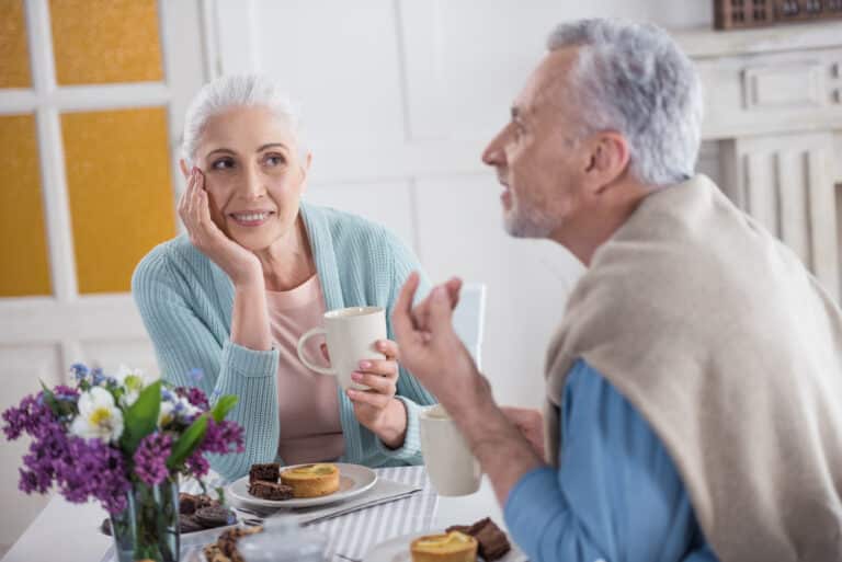 Senior man talkng over breakfast, senior woman smiling at him