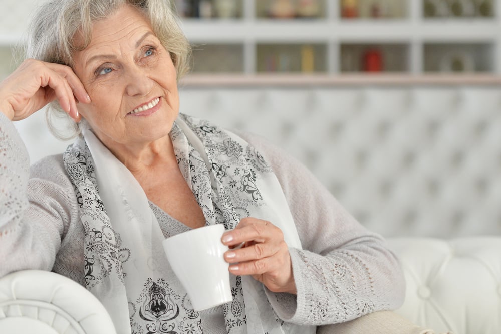 Smiling senior woman looking thoughtful, holding mug, sitting on couch