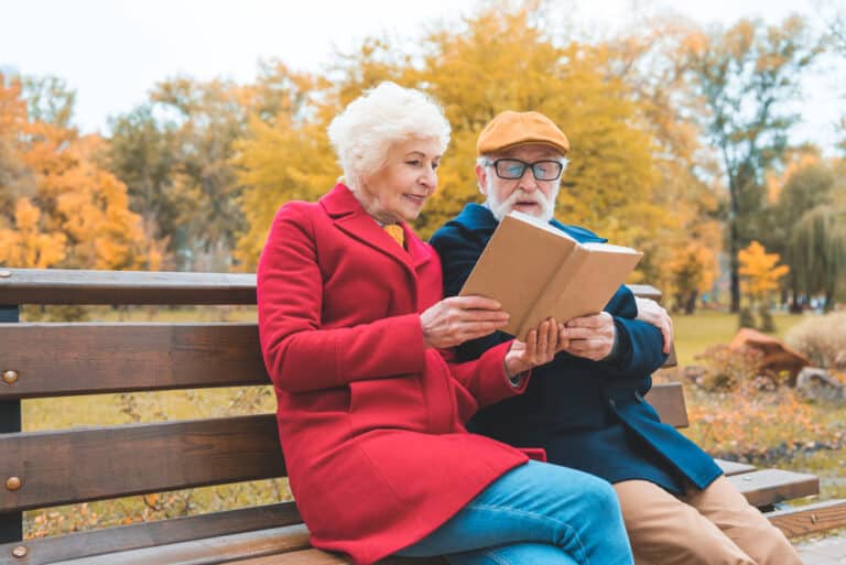 senior couple reading book in the park in fall
