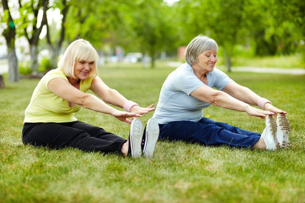 Two smiling senior women touching their toes in the grass