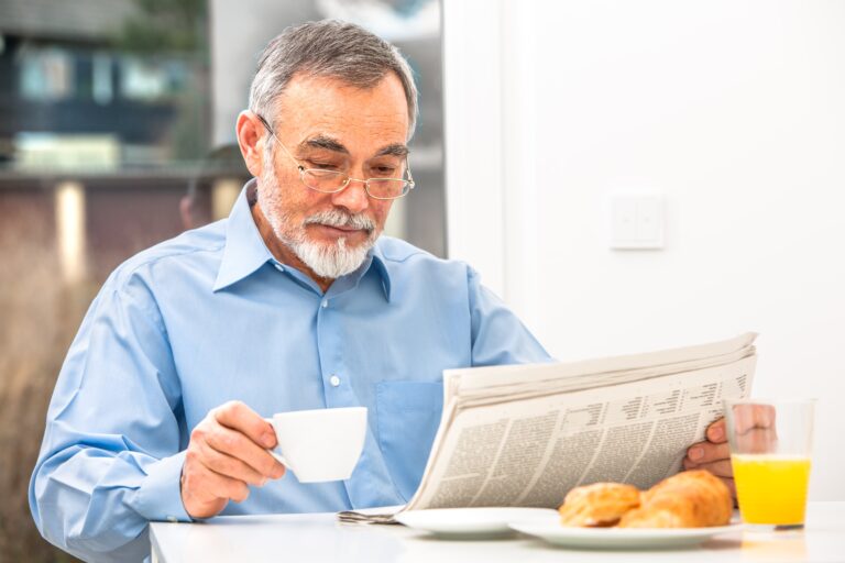 senior man reading newspaper and drinking coffee