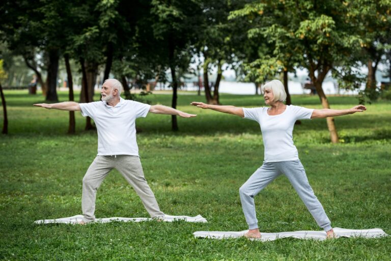 senior couple performing warrior II pose outside on yoga mats