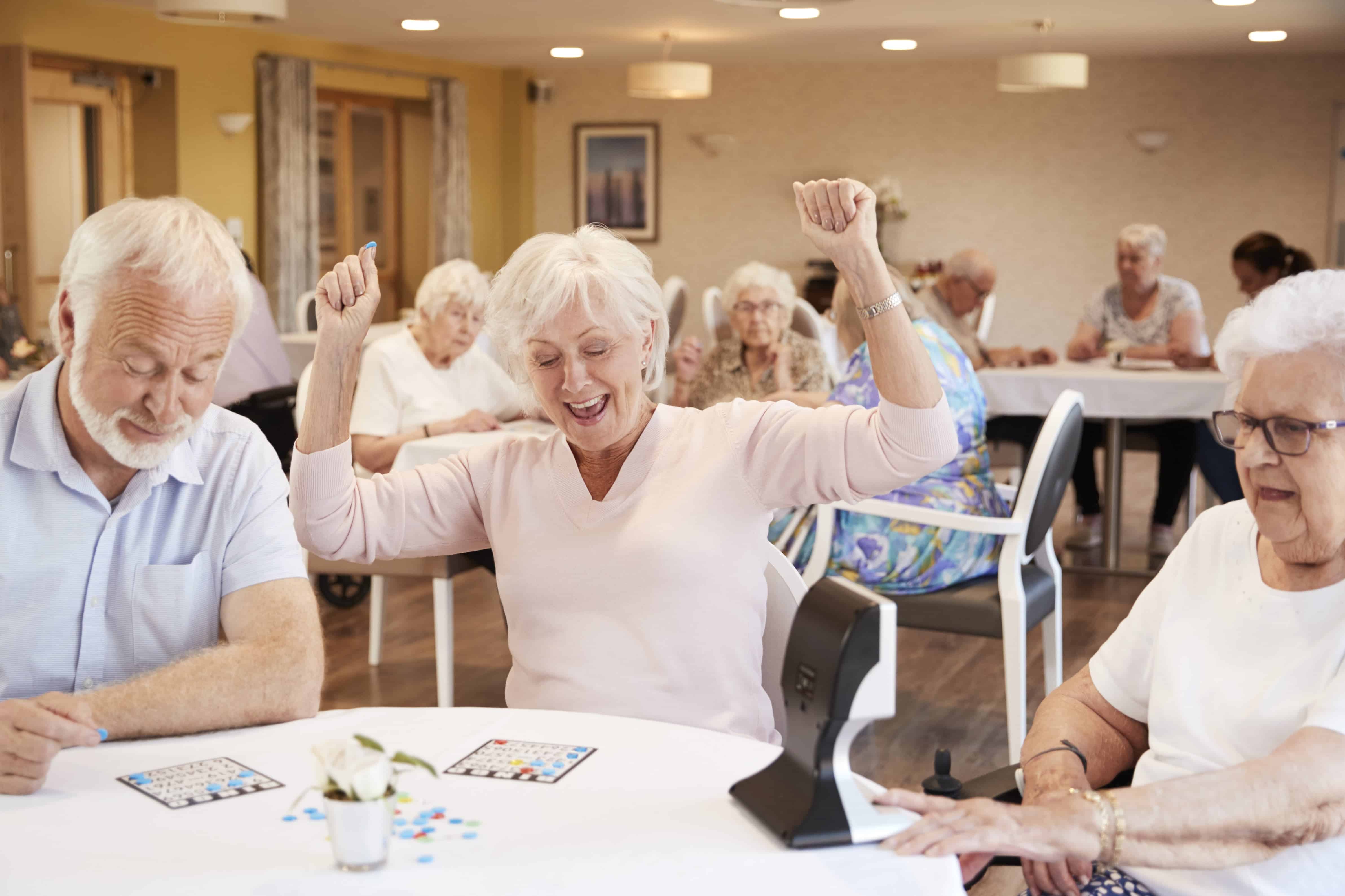 Seniors playing bingo, woman raising her hands in triumph