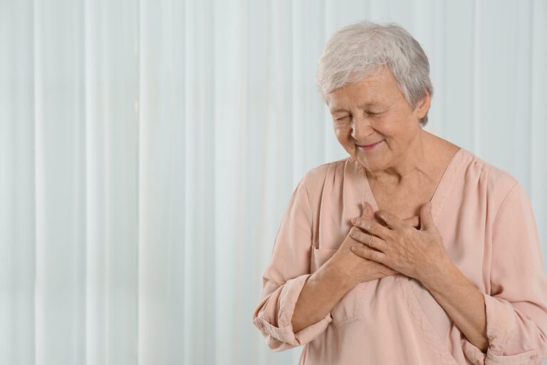 Senior woman touching hands to her chest, looking pleased