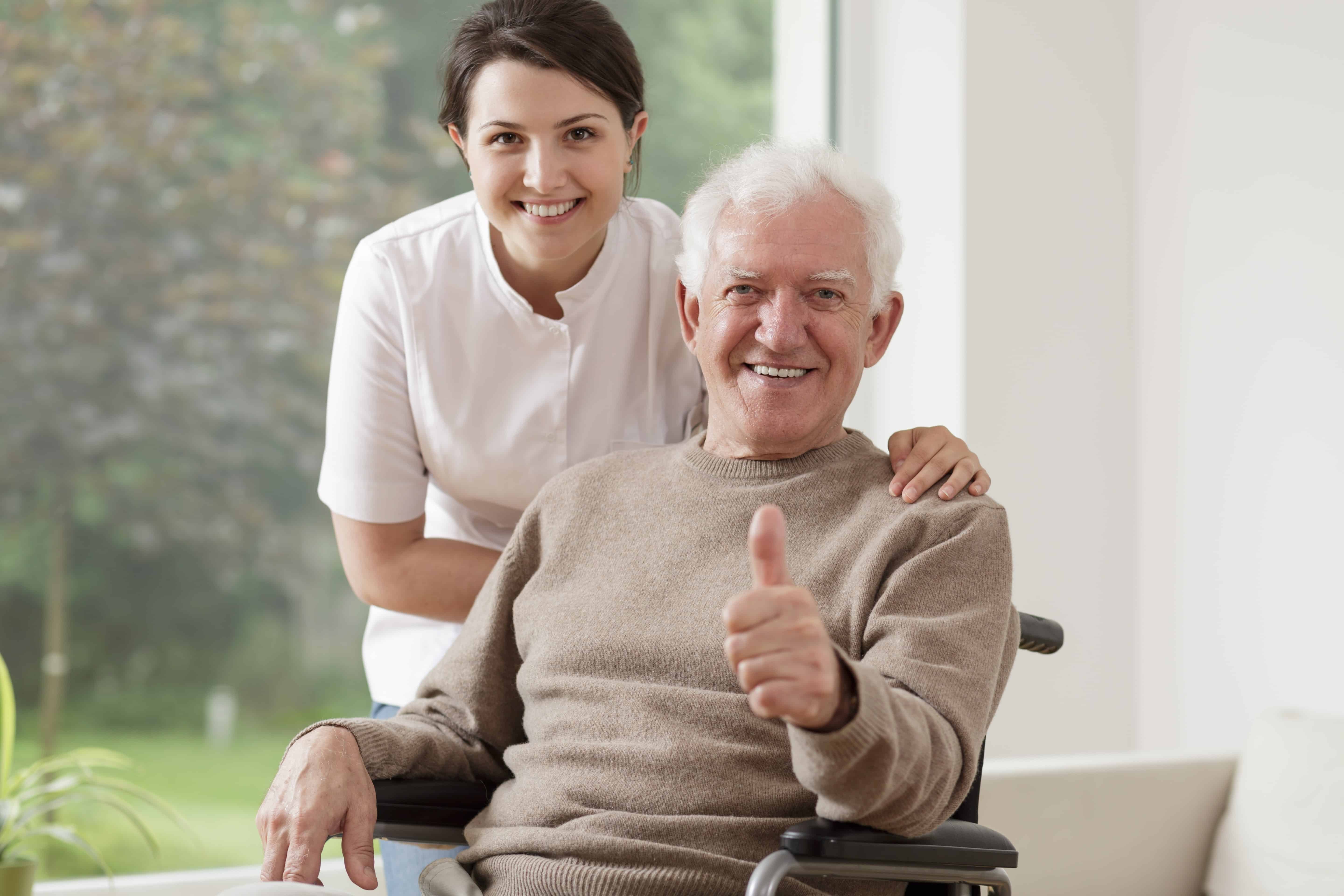 Smiling senior man giving thumbs up to camera, smiling nurse behind him